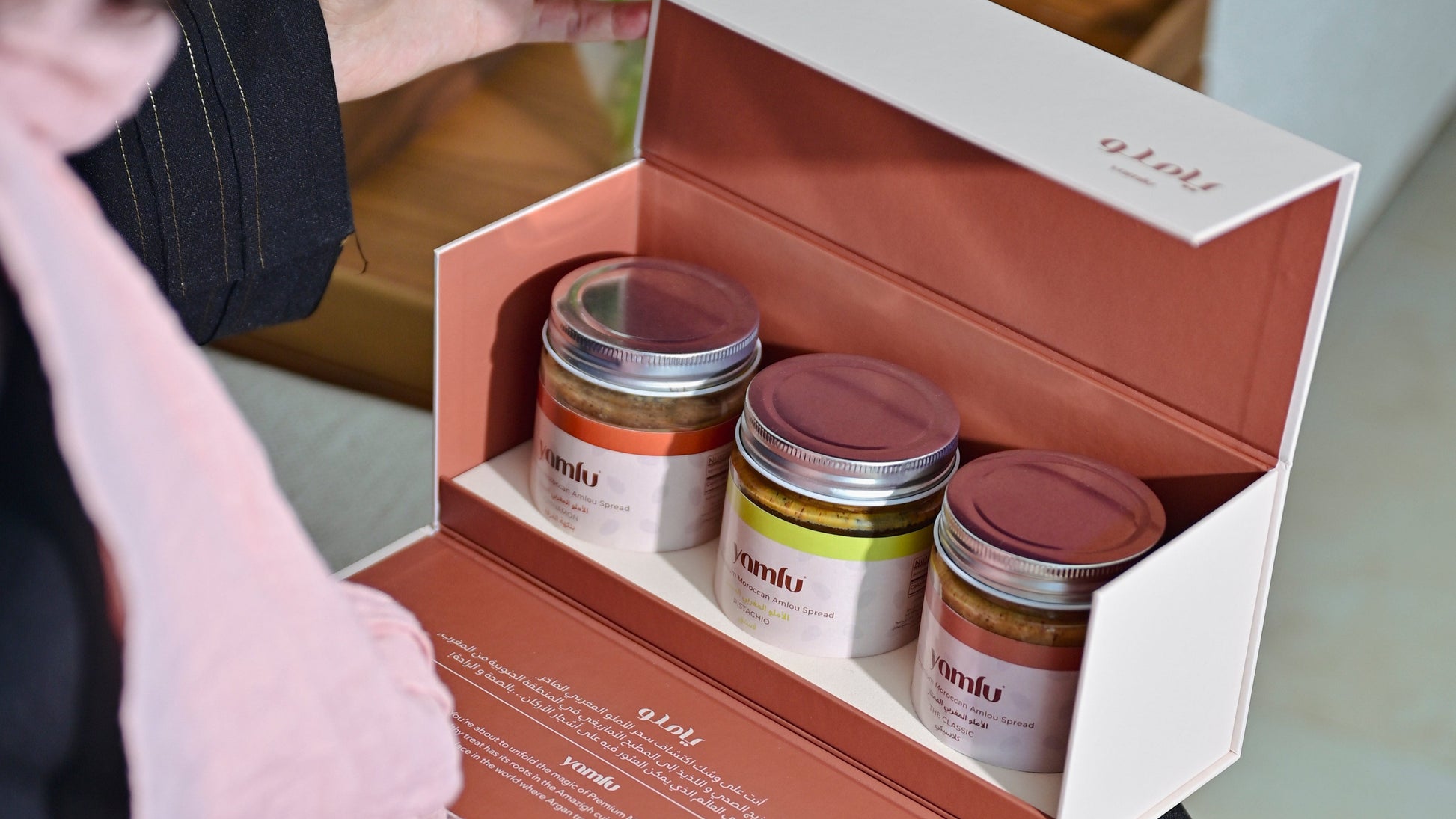 Person opening a box containing three small jars with lids.